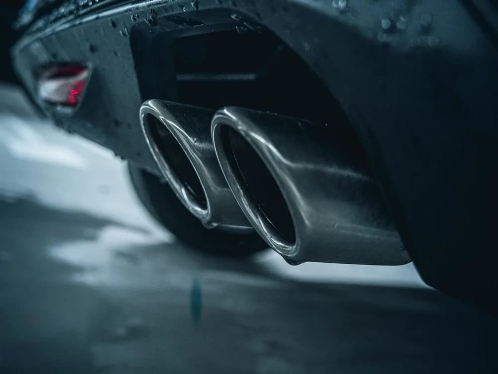 Twin exhaust tips on a dark car, beaded with rain